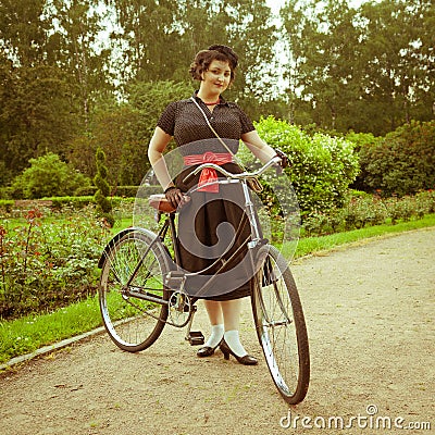 Young woman in dress posing with retro bicycle in the park.