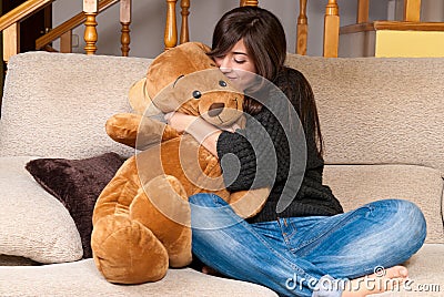 Young woman embracing teddy bear sitting on sofa