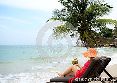 Young woman enjoys young coconut sitting on the beach