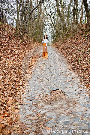 Young woman far outdoors in the autumn park among fallen leaves