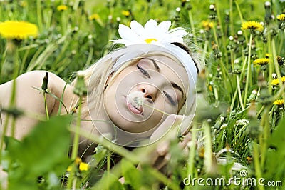 Young woman with flower in her hair blowing on a dandelion.