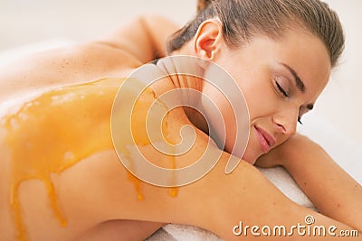 Young woman with honey on back laying on massage table