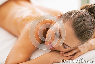 Young woman with honey on back laying on massage table