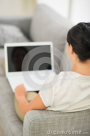 Young woman laying on couch and working on laptop
