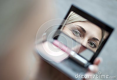 Young woman looking in cosmetic mirror