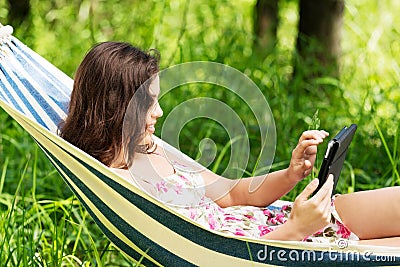 Young woman lying in a hammock in garden with E-Book.