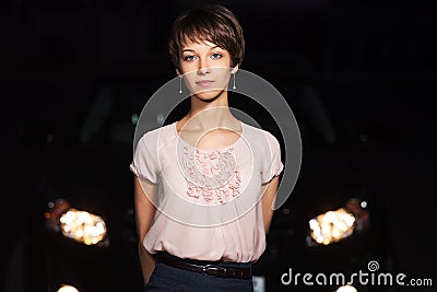 Young woman in the night in front of car headlights