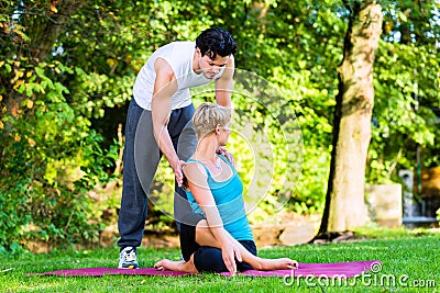 Young woman outdoors doing yoga with trainer