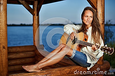 Young woman playing guitar in summerhouse