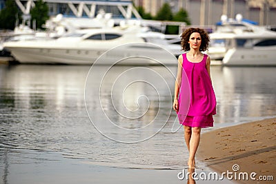 Young woman in a red dress and curly hair on the water coast