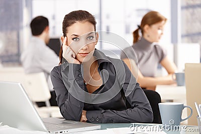 Young woman sitting at desk others working behind