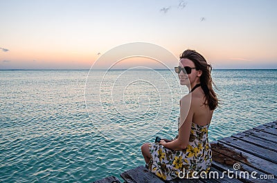 Young woman sitting on seaside jetty at sunset