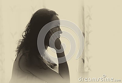 Young woman sitting and thinking near bright window light. black and white filtered image.