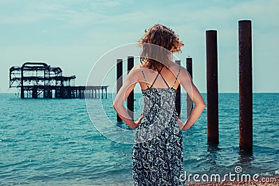 Young woman standing by the ocean with old pier