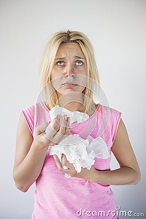 Young woman suffering from cold looking up while holding tissues against gray background