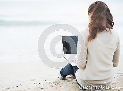 Young woman in sweater sitting on lonely beach and