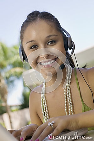 Young woman using laptop and headset at table in back yard portrait