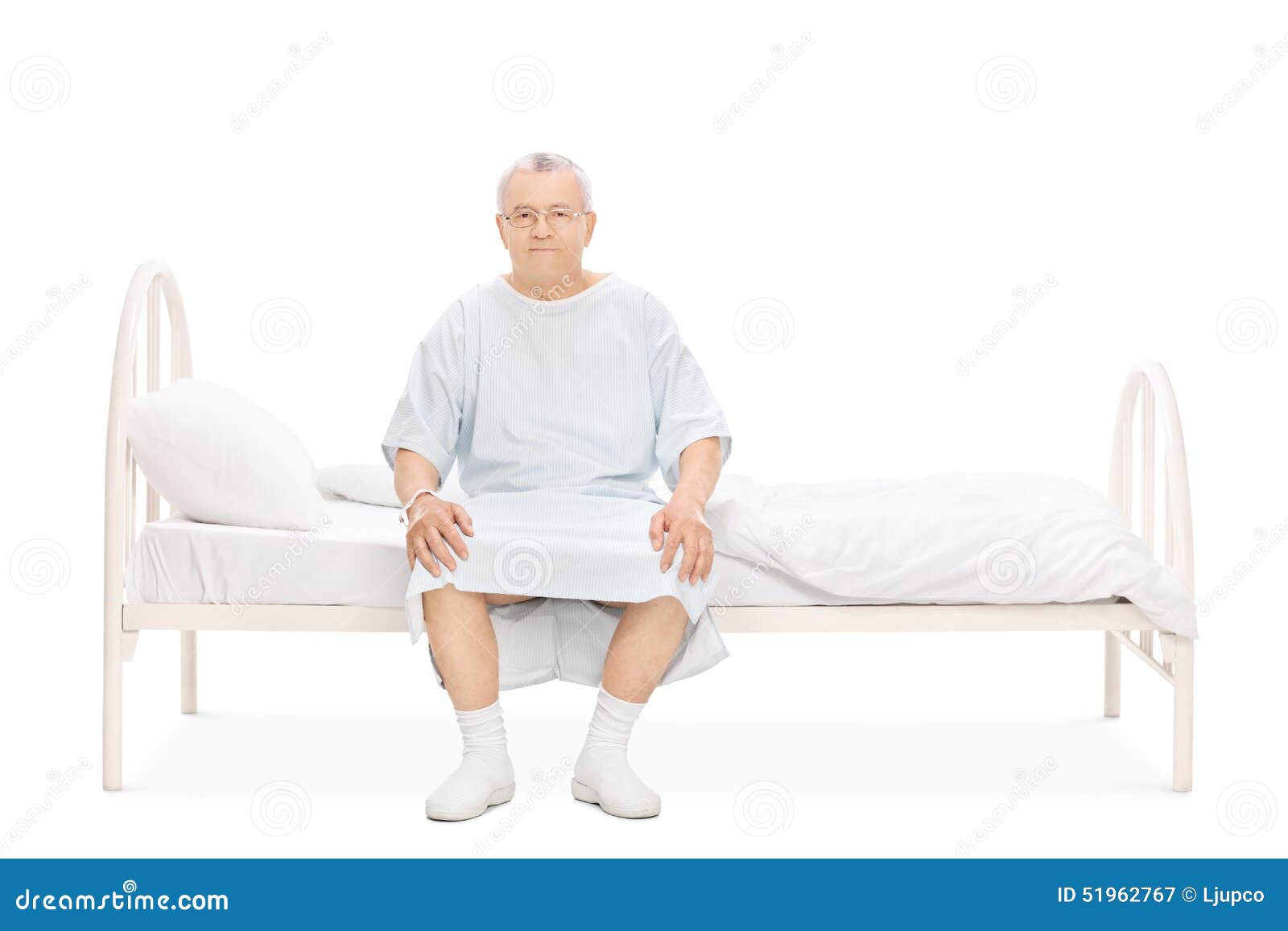 坐床和看照相机的医院褂子的成熟患者被隔绝在白色背景.图片