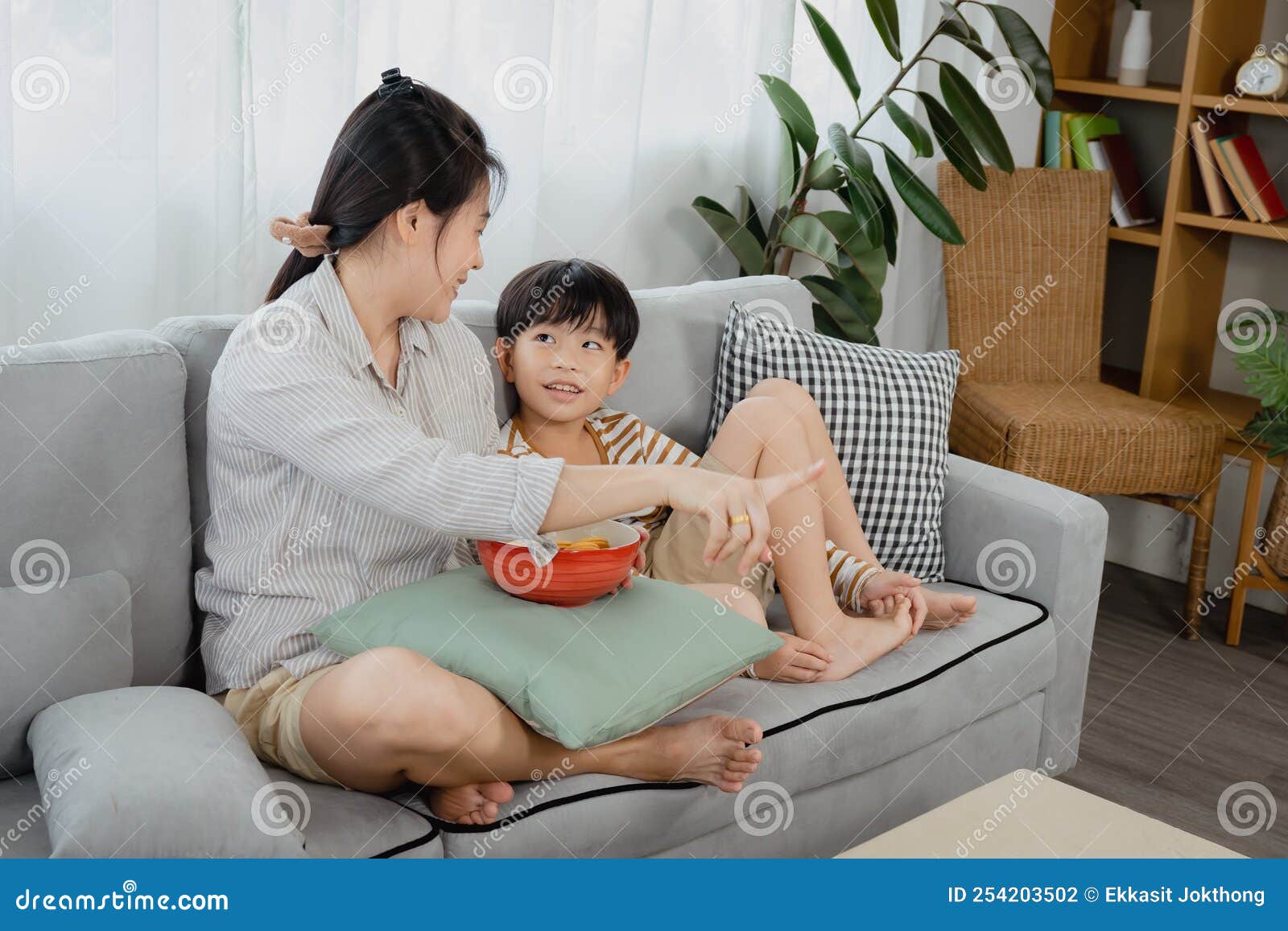 An Asian Single Mom And His Son Watch Tv On The Sofa In The Living Room