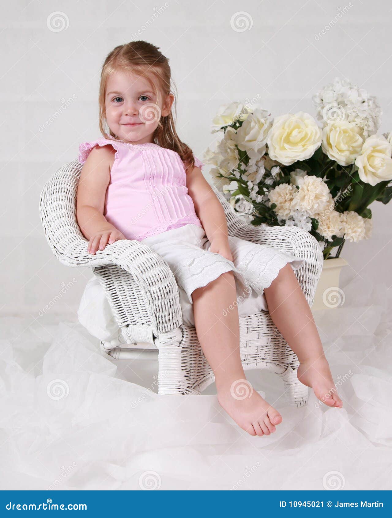  this beautiful little girl smiles as she sits in a white wick chair