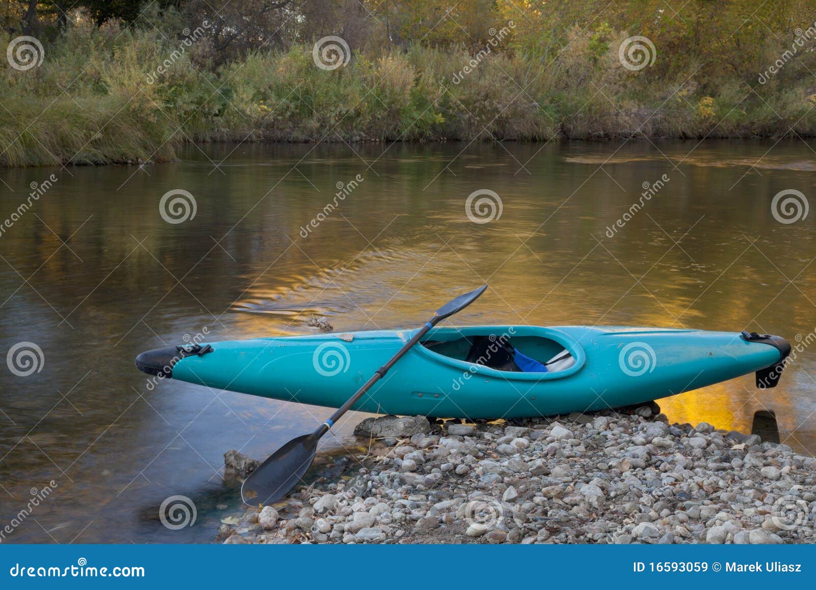 Blue whitewater kayak on a rocky shore against river with gold color 