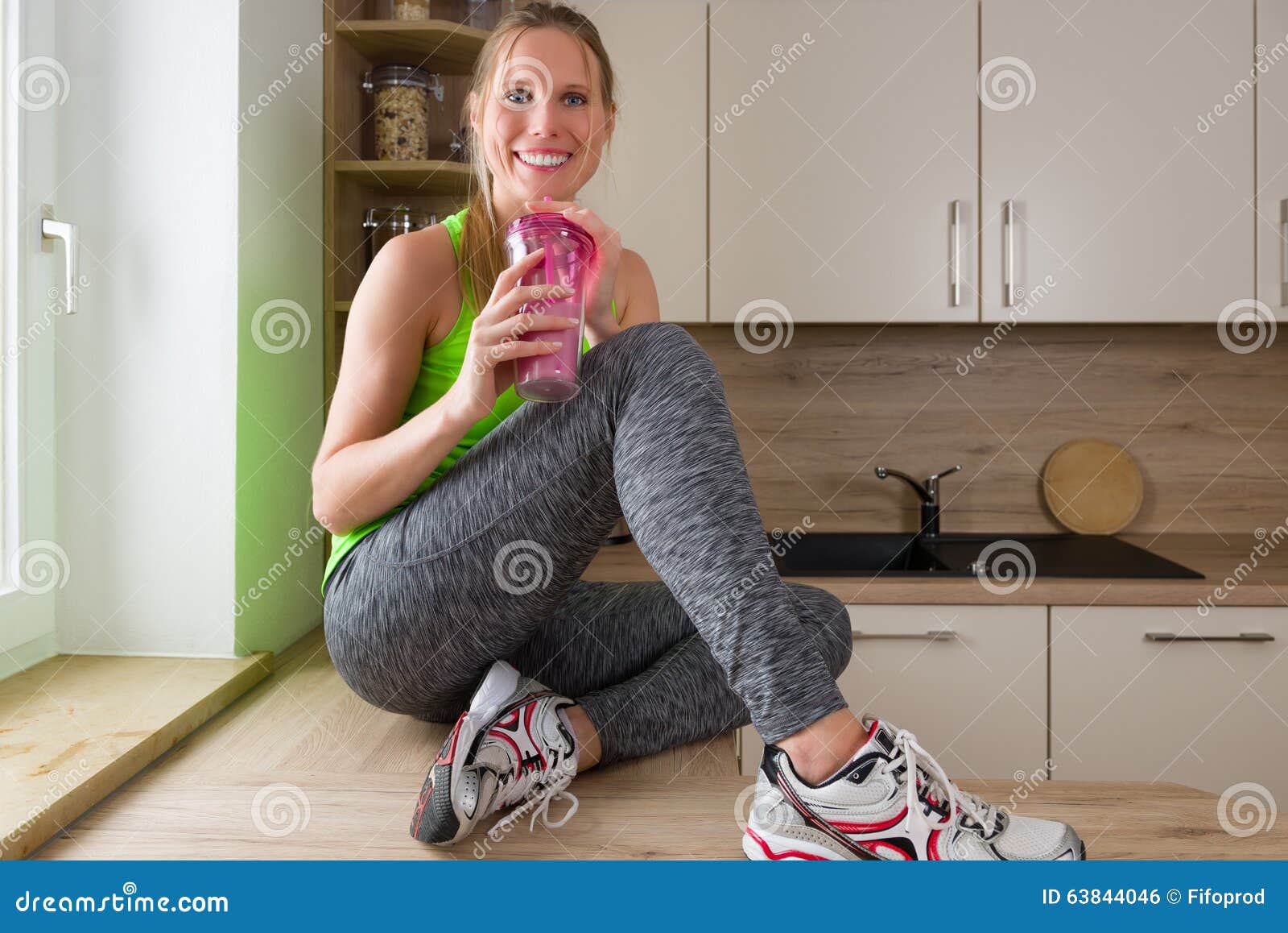 Caucasian Woman In Gym Suit Drinking Protein Shake In The Kitchen Stock