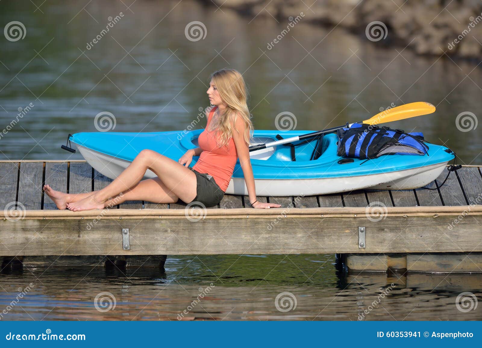by her kayak on a floating dock on lake - lit by early morning sun
