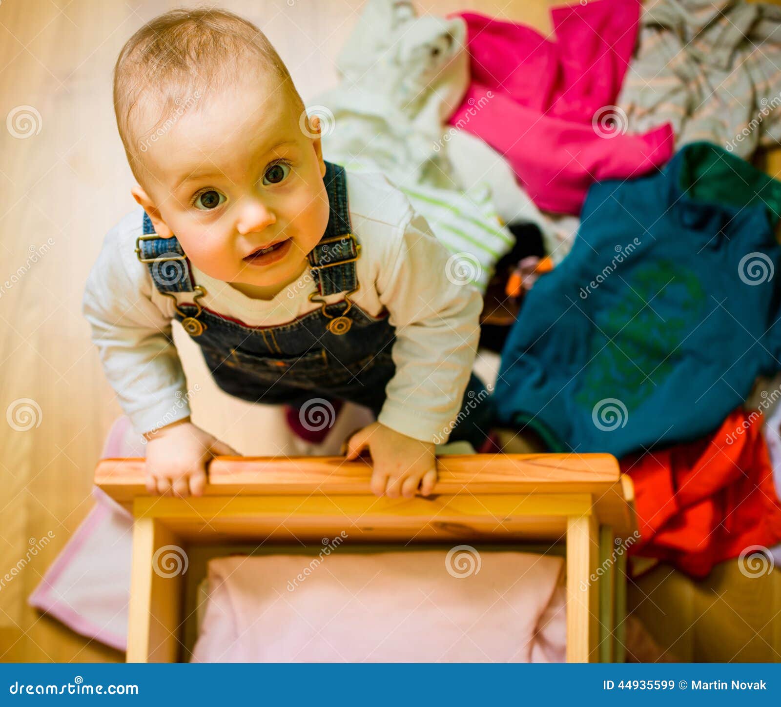 Baby throws out clothes from wooden furniture at home.