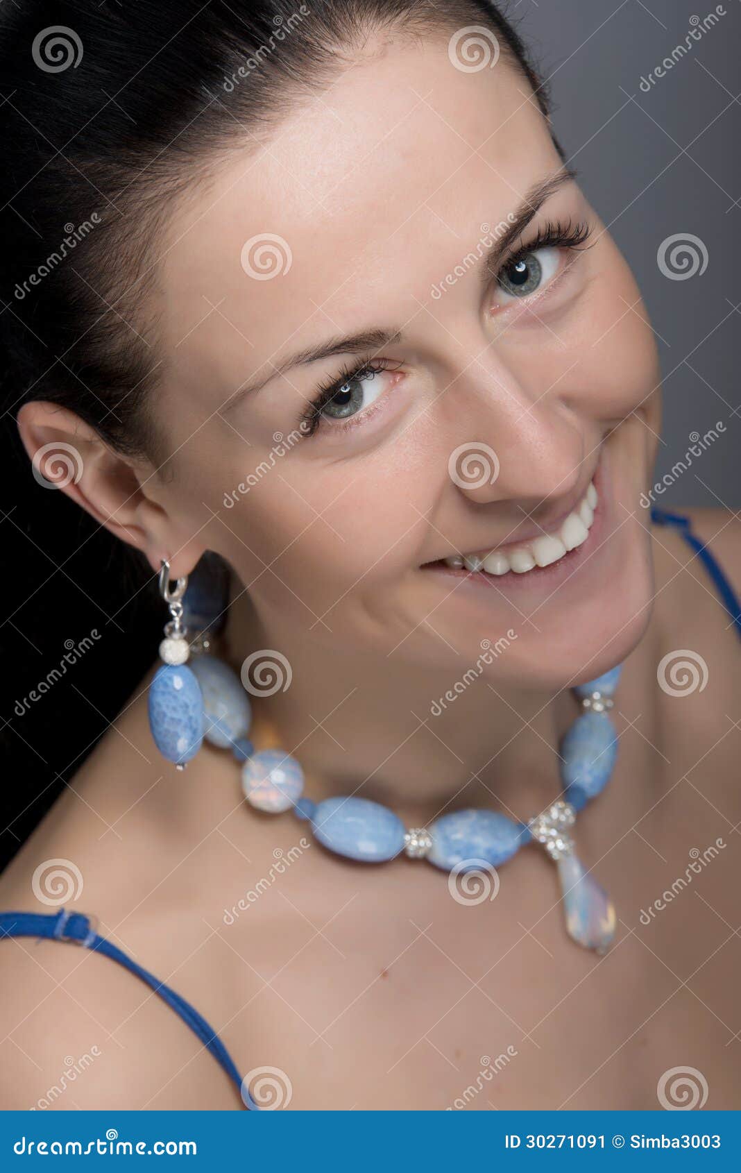 Feche acima do retrato de brincos da mulher e da colar vestindo de sorriso felizes novos da luz - pedras azuis. Cara natural da beleza. Foco seletivo. - feche-acima-do-retrato-de-brincos-da-mulher-e-da-colar-vestindo-de-sorriso-felizes-novos-da-luz-pedras-azuis-cara-natural-da-30271091