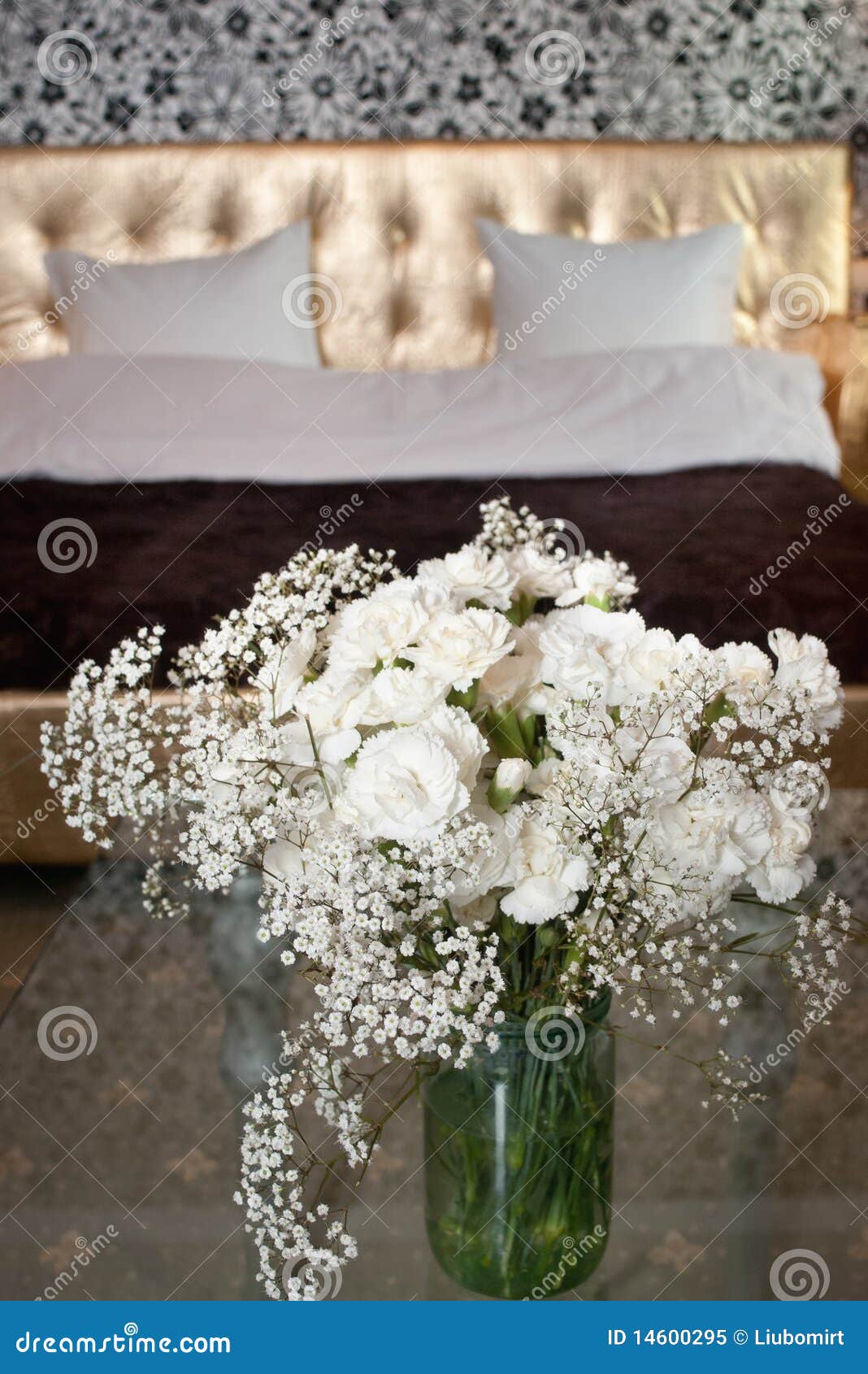 White fresh flowers in bowl with blurred bed with two pillows.