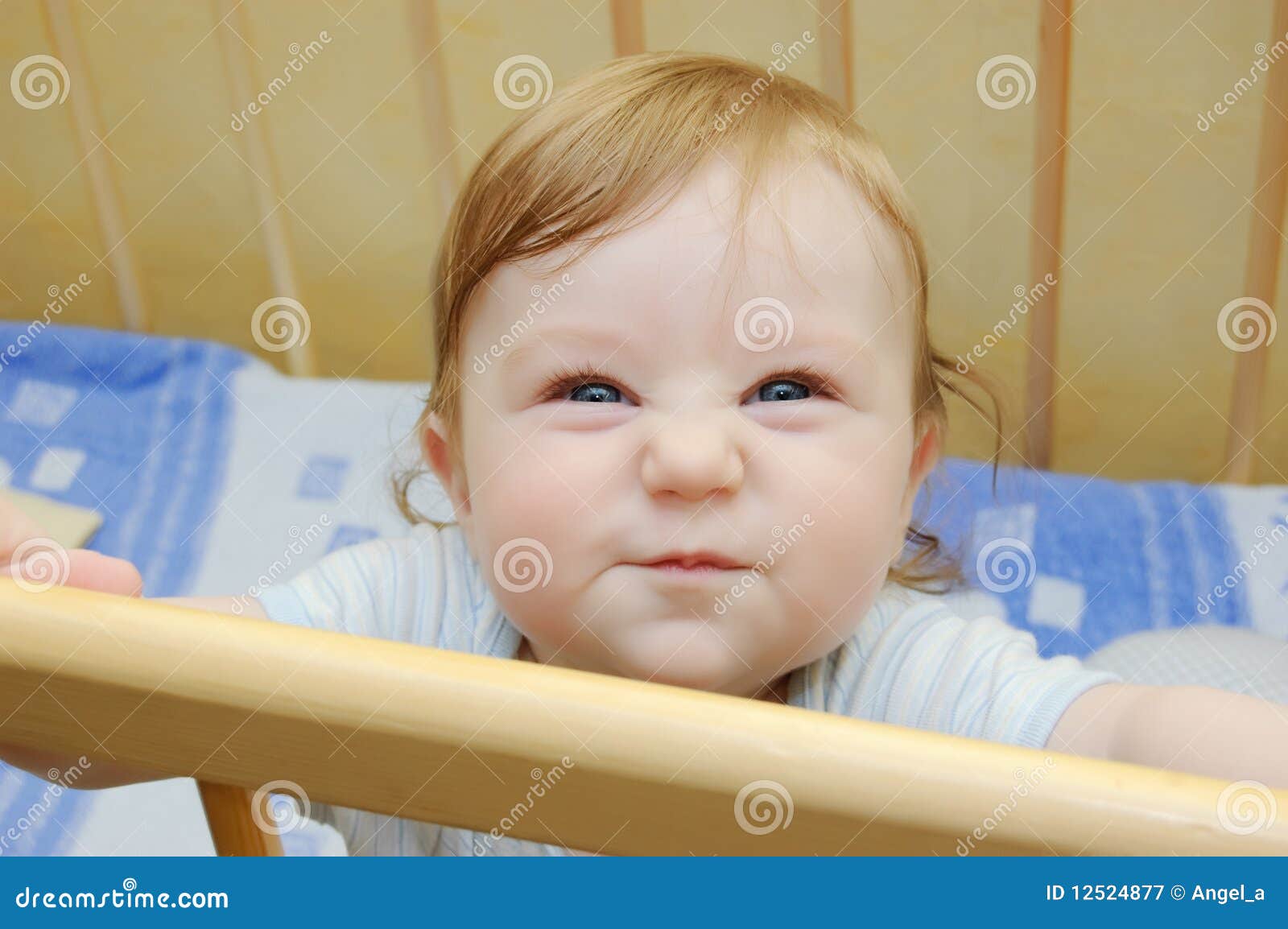 Funny grimace on baby boy face sitting in bed.