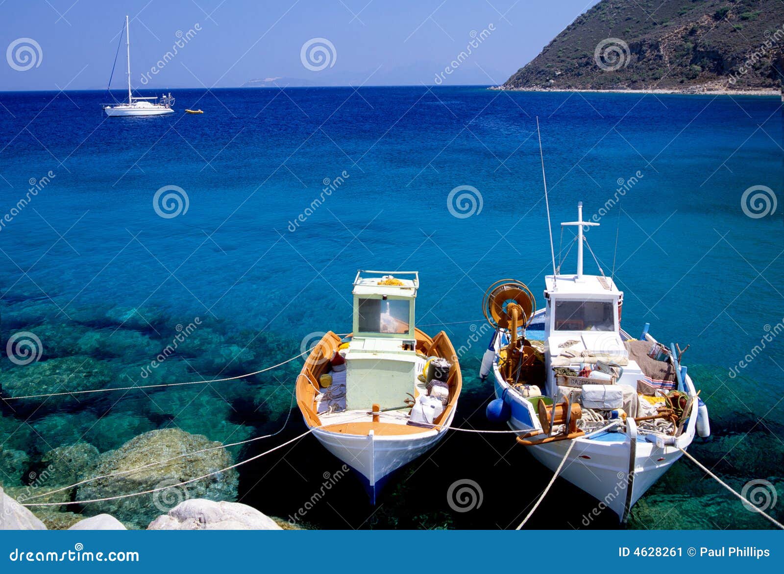 Two greek fishing boats with a sailboat passing.