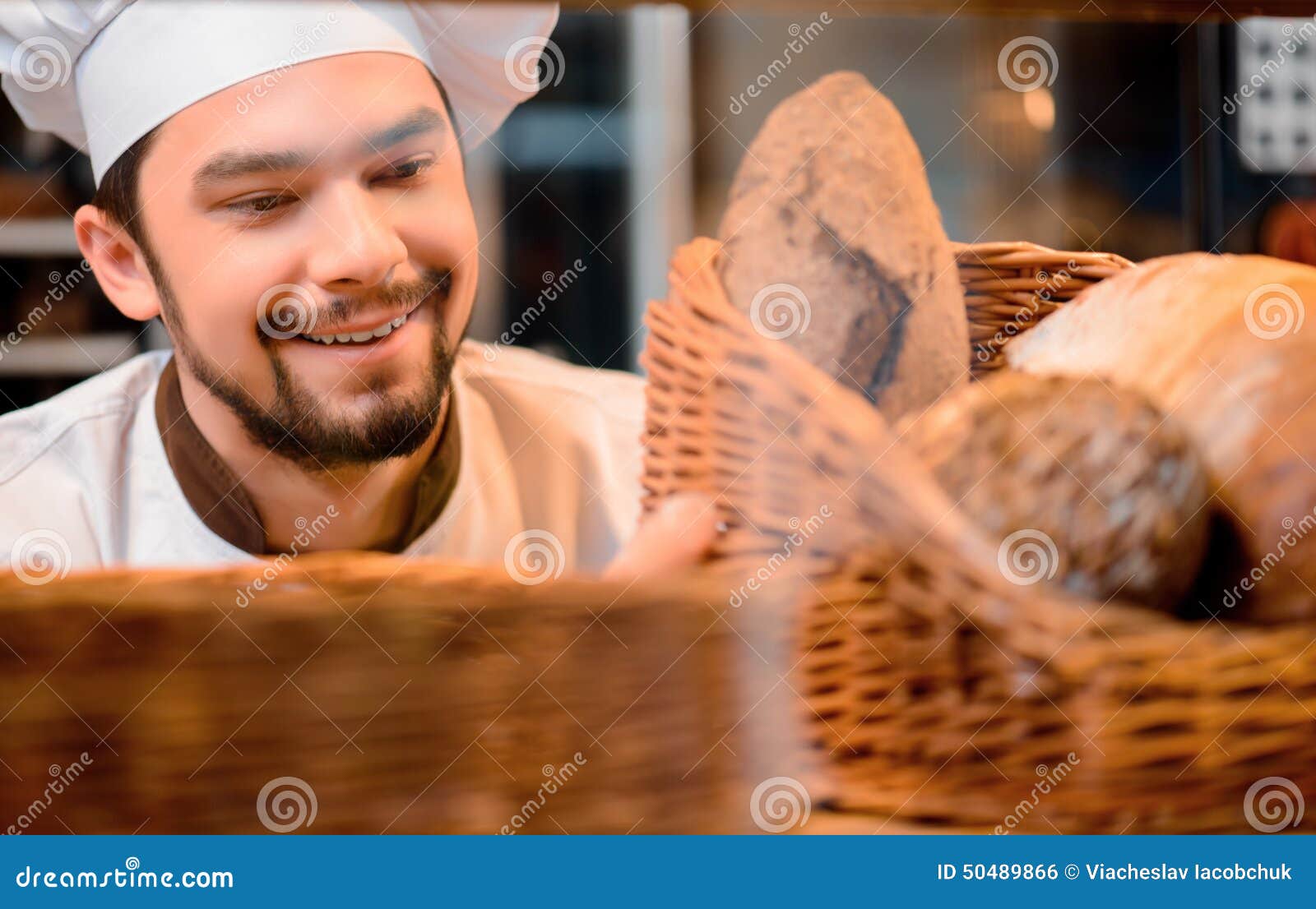 Handsome cook in the kitchen - handsome-cook-kitchen-proud-his-baked-goods-cropped-image-young-man-uniform-looking-basket-baked-goods-50489866