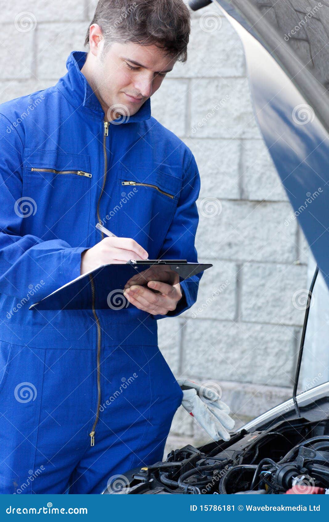 Handsome mechanic writing on a clipboard standing in front of a car at ...