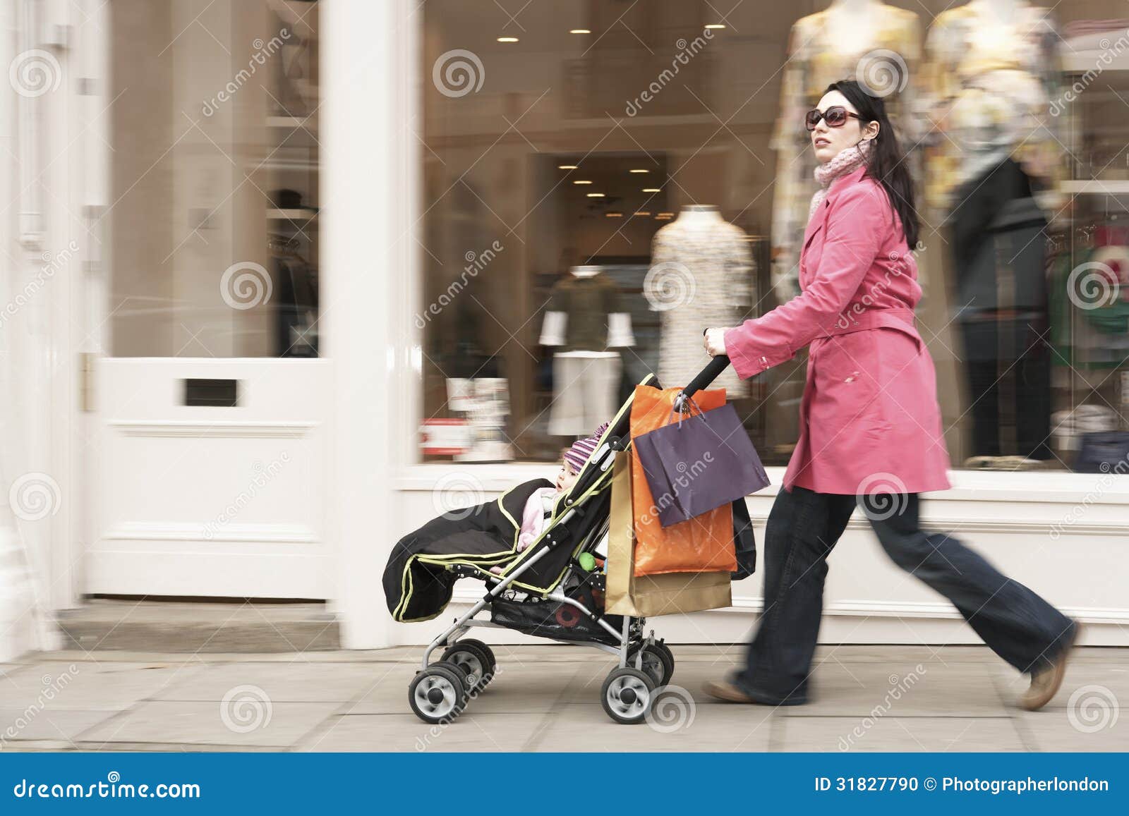side view of young mother pushing baby stroller by clothes shop