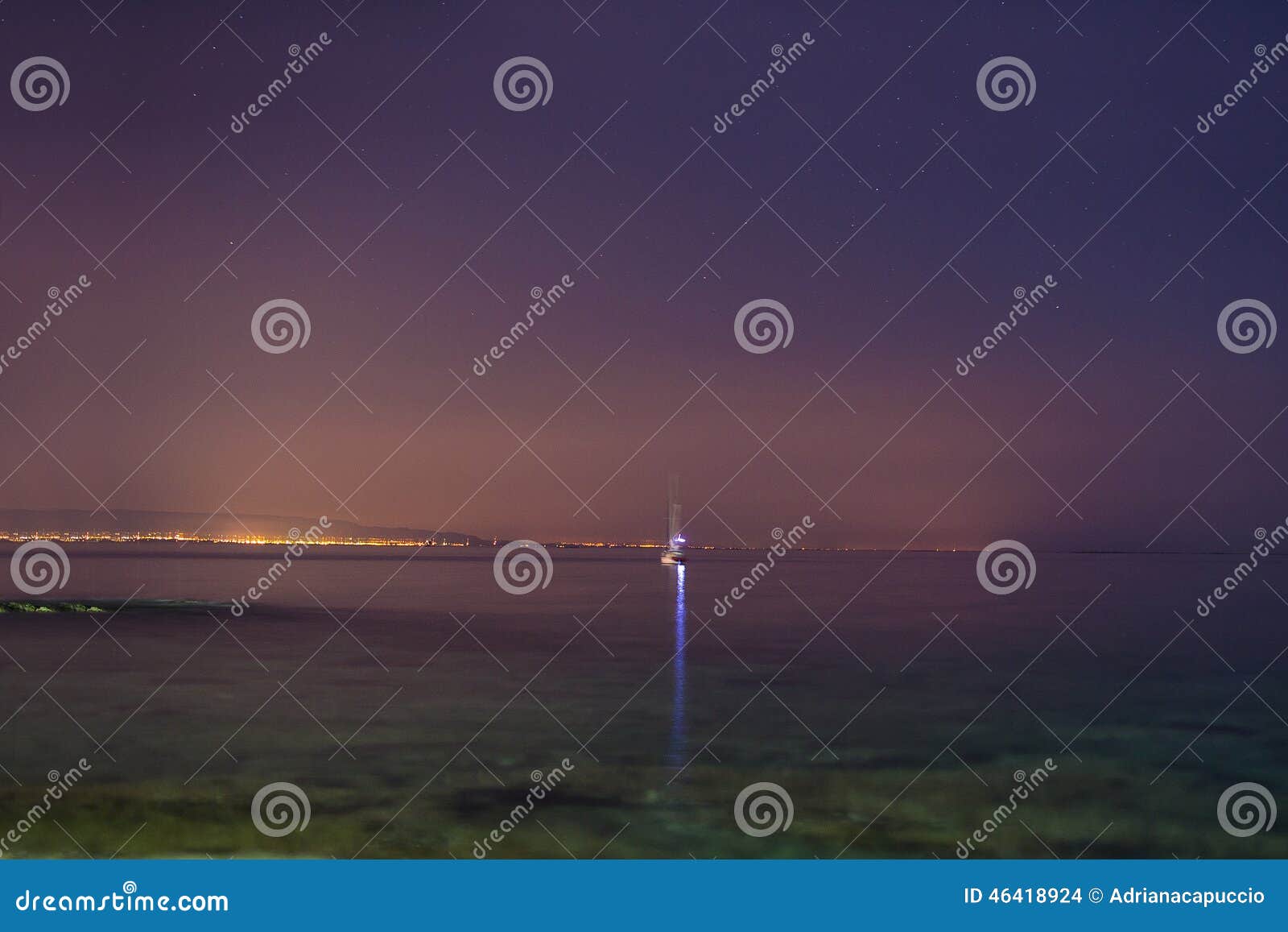 View of the ocean at night with a fishing boat on the horizon.