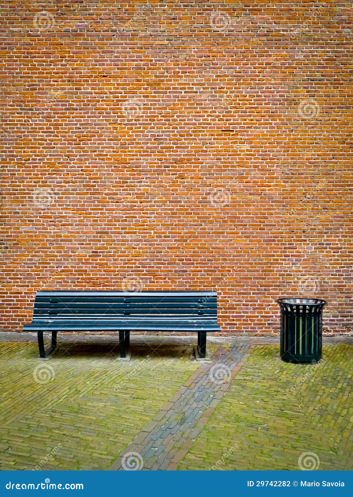 Old black bench and trashcan in front of a red brick wall.