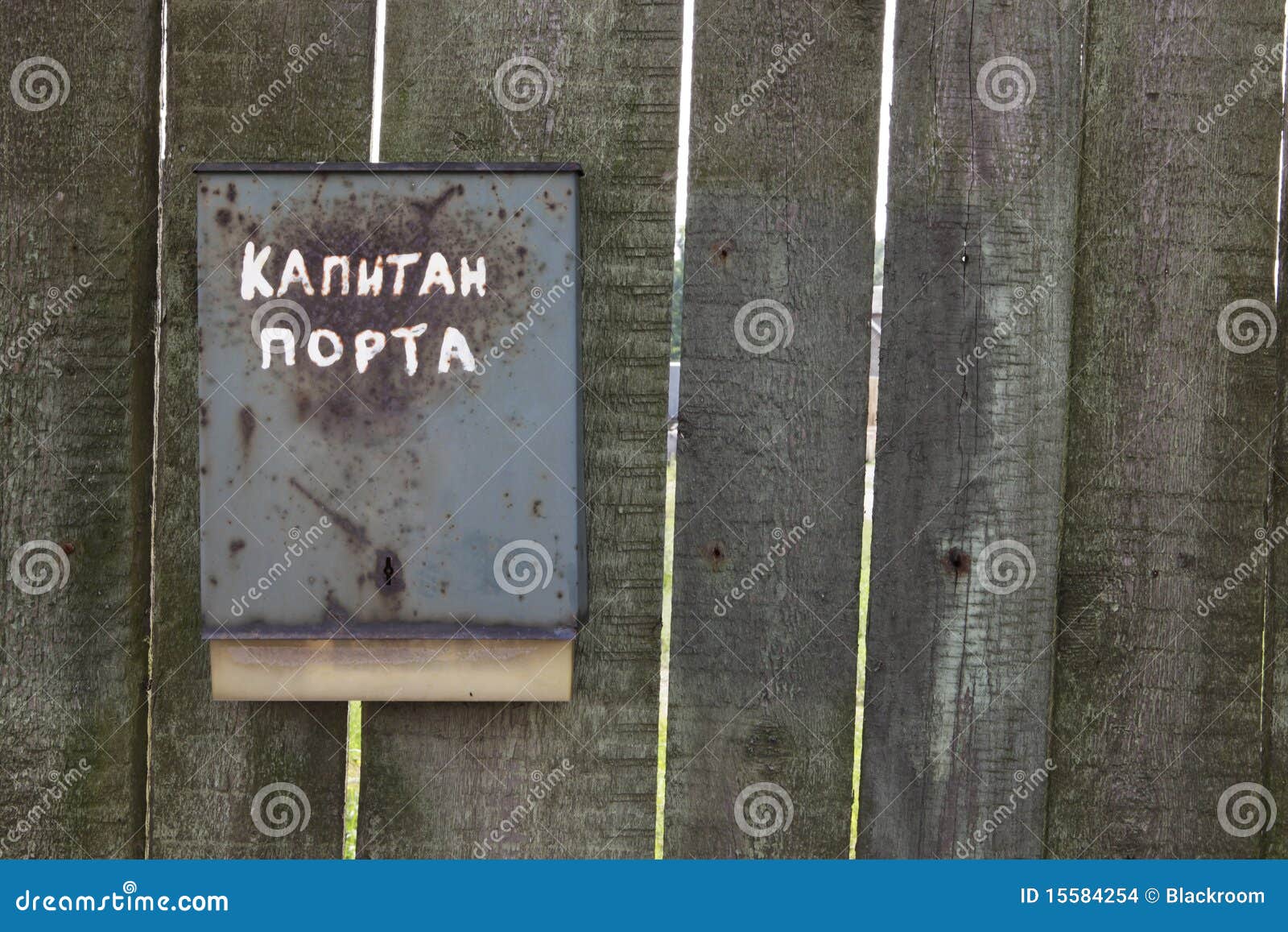 Old rusty mailbox with russian sign on it, on old wooden fence.