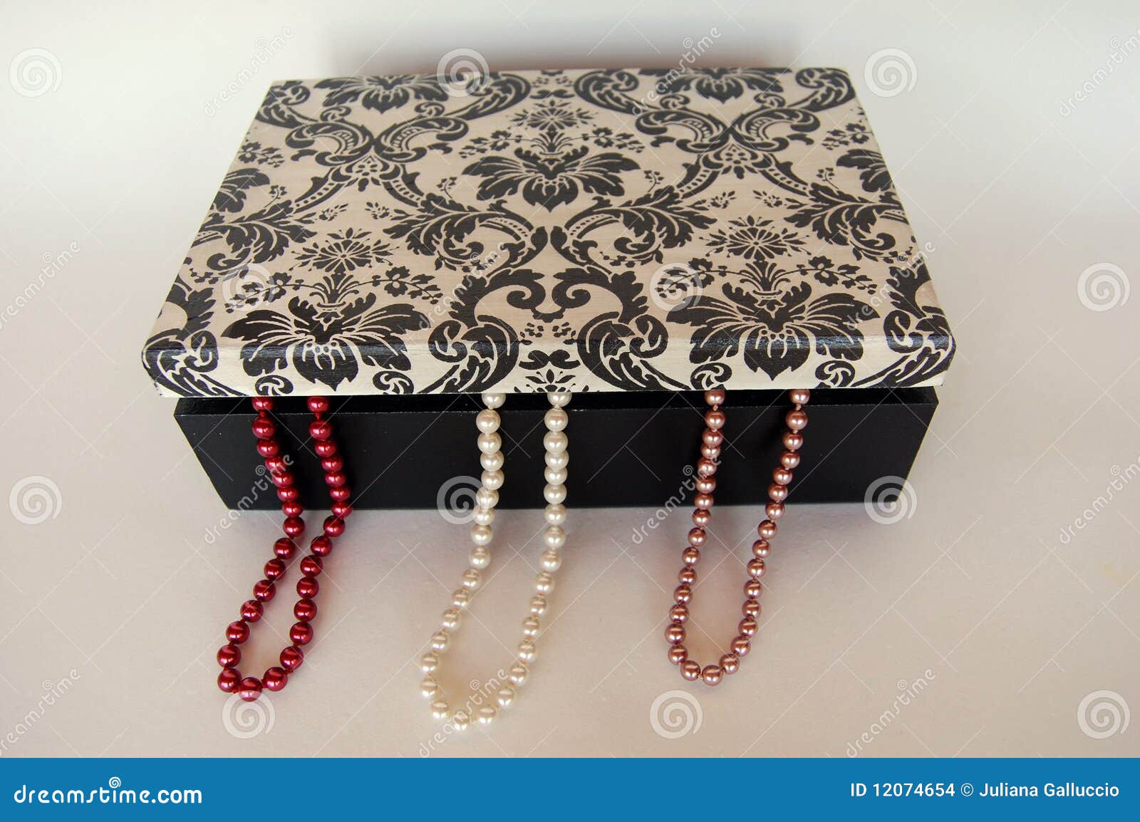 Three colorful pearl necklaces hanging out of a jewelry box. .