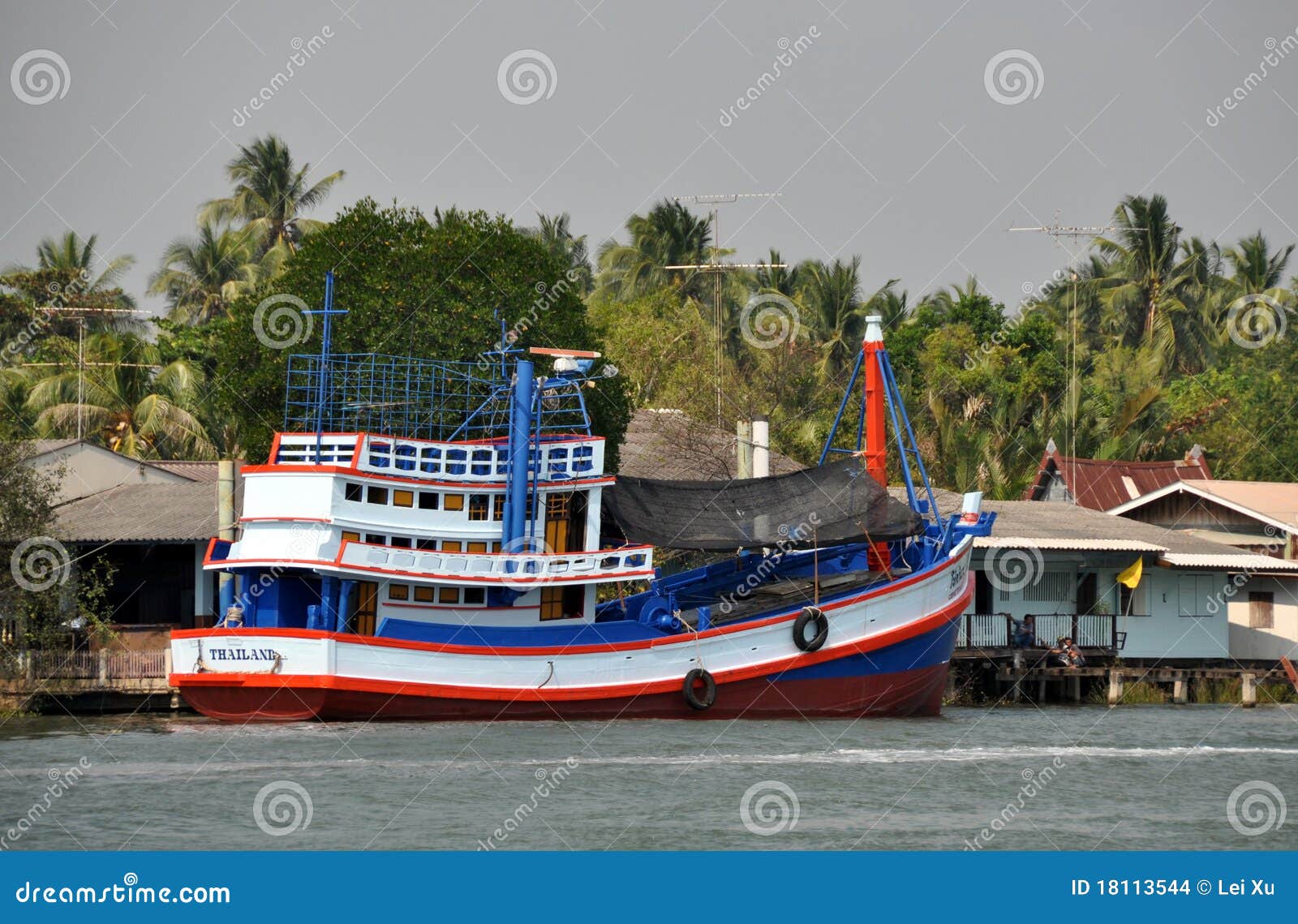 large fishing vessel steams past old wooden houses lining the banks 