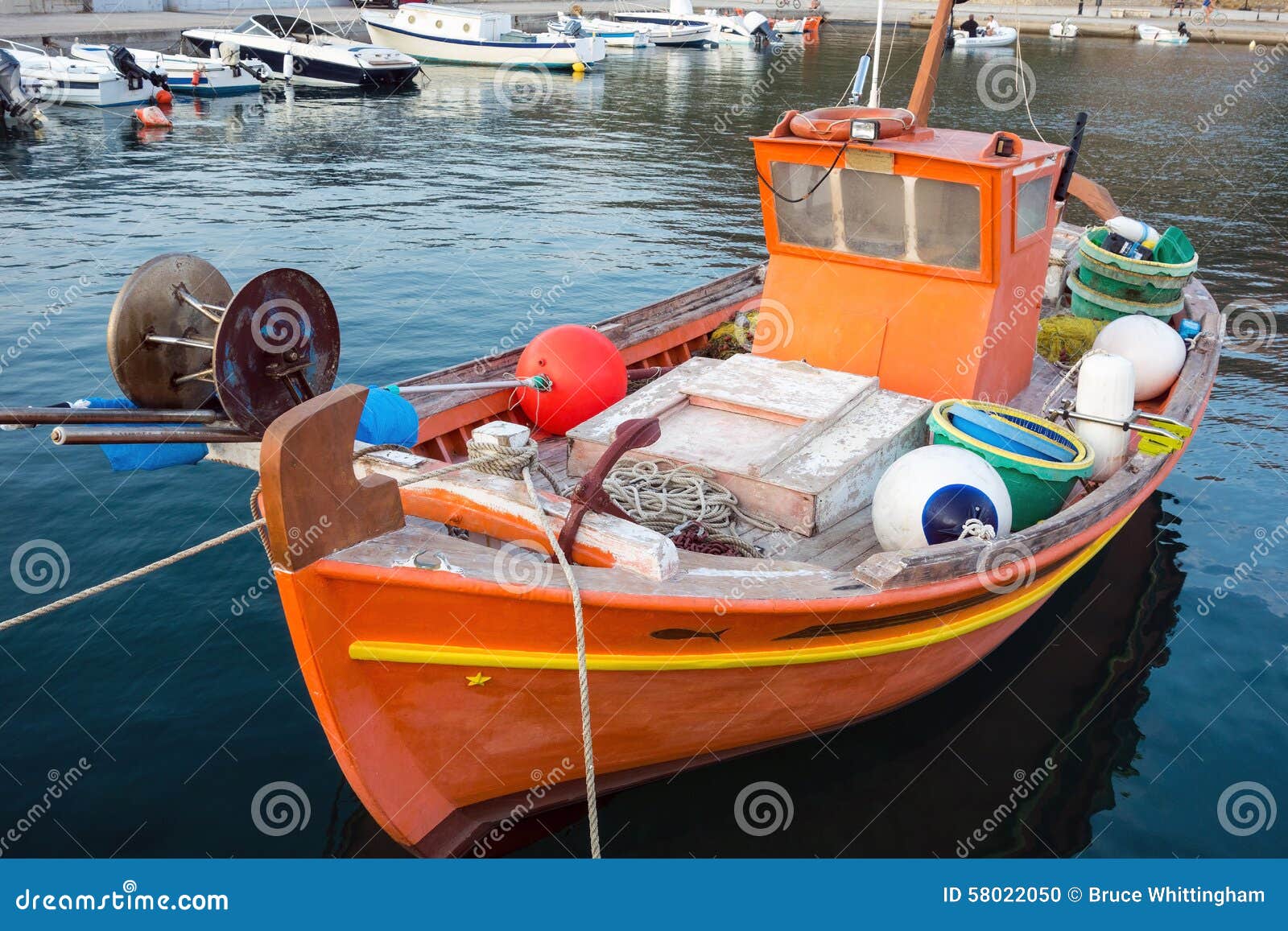 Small orange painted wooden fishing boat, or caique, moored in Greek 