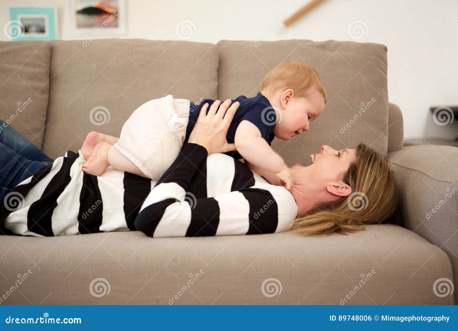 Smiling Mother Lying On Sofa At Home And Playing With Her Son Stock