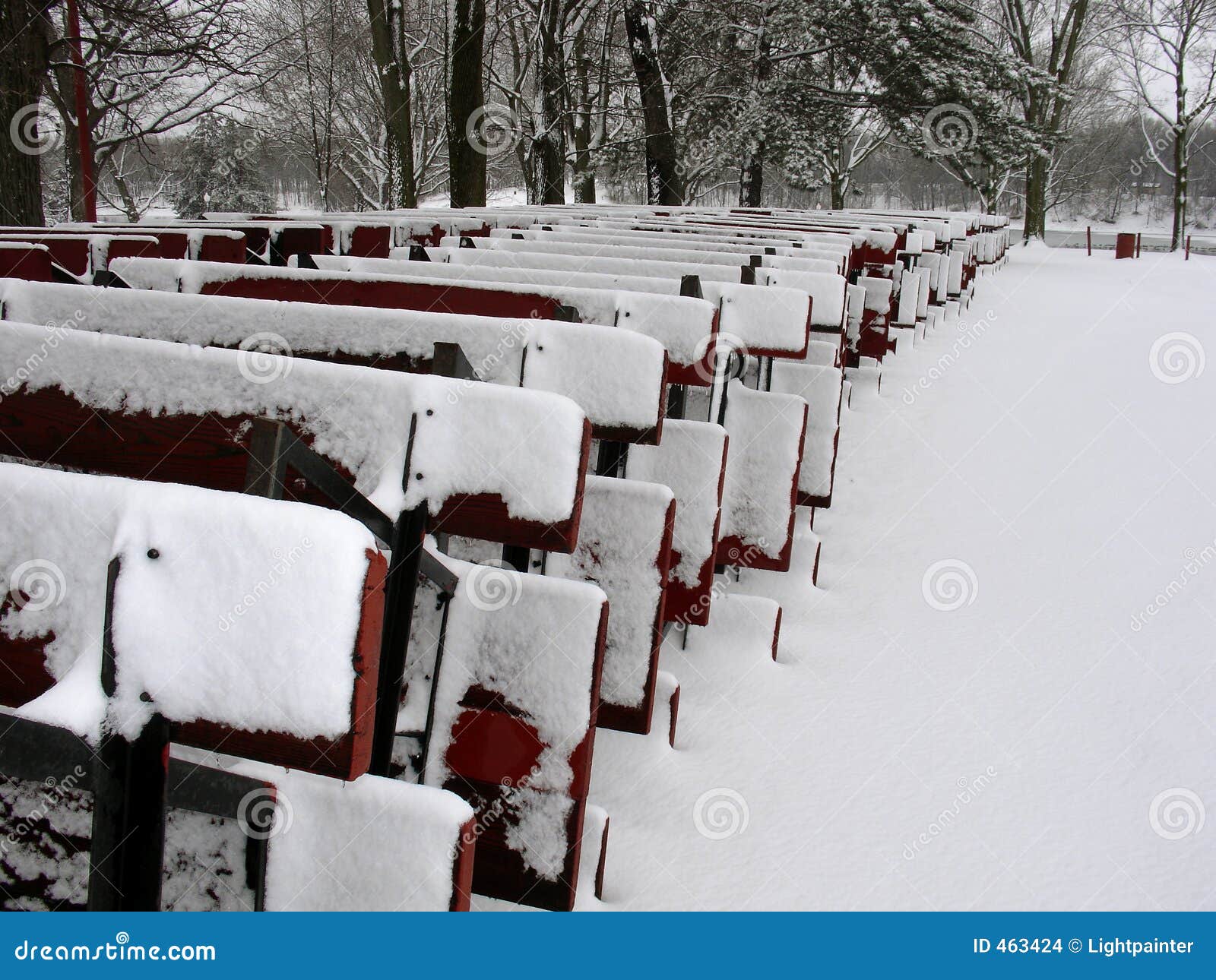 Row of snow covered wooden picnic tables or benches stored in park.