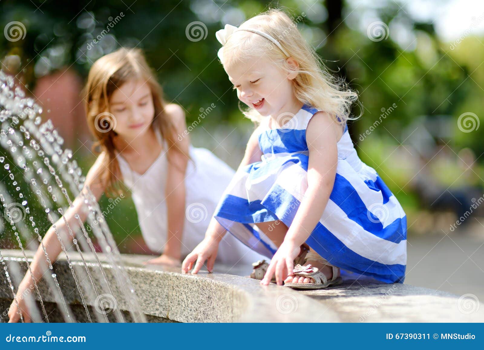 Two Cute Little Girls Playing With A City Fountain On Hot Summer Day