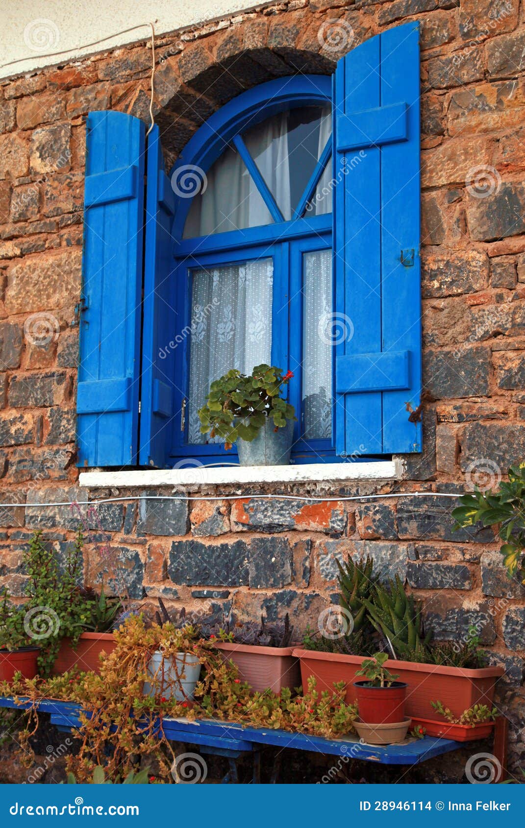 Vintage blue window with shutter and flower pot set in old stone wall 