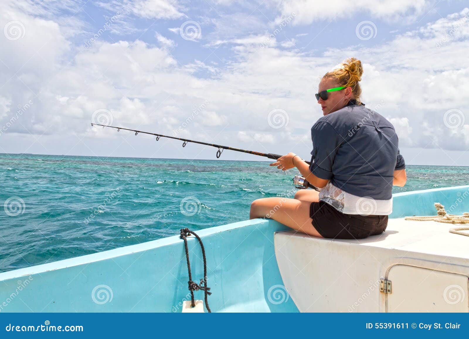 Woman deep sea fishing from the side of a boat on the ocean under blue ...