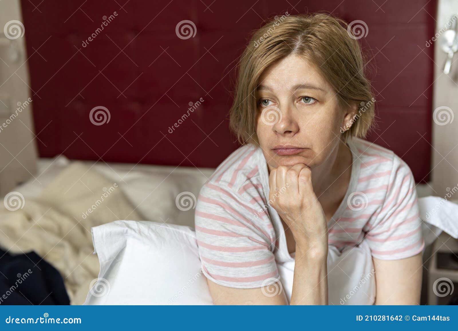 A Sad Pensive Middle Aged Mature Woman Sits On A Bed In A Bedroom