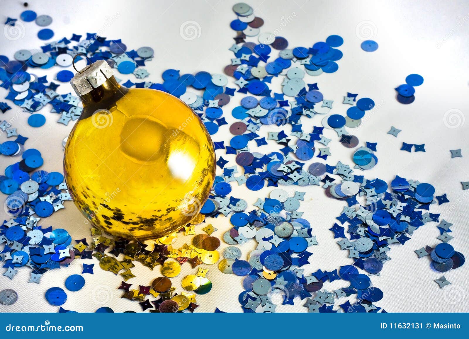 Yellow christmas-tree decoration with blue confetti over white.