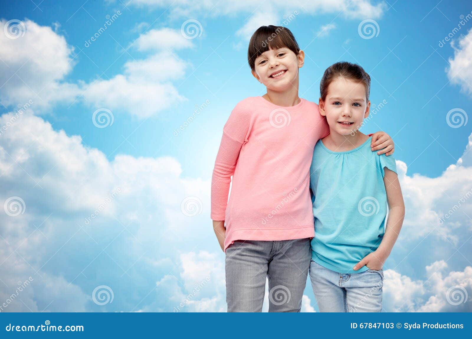 童年,时尚,友谊和人概念-拥抱在蓝天和云彩背景的愉快的微笑的小女孩.