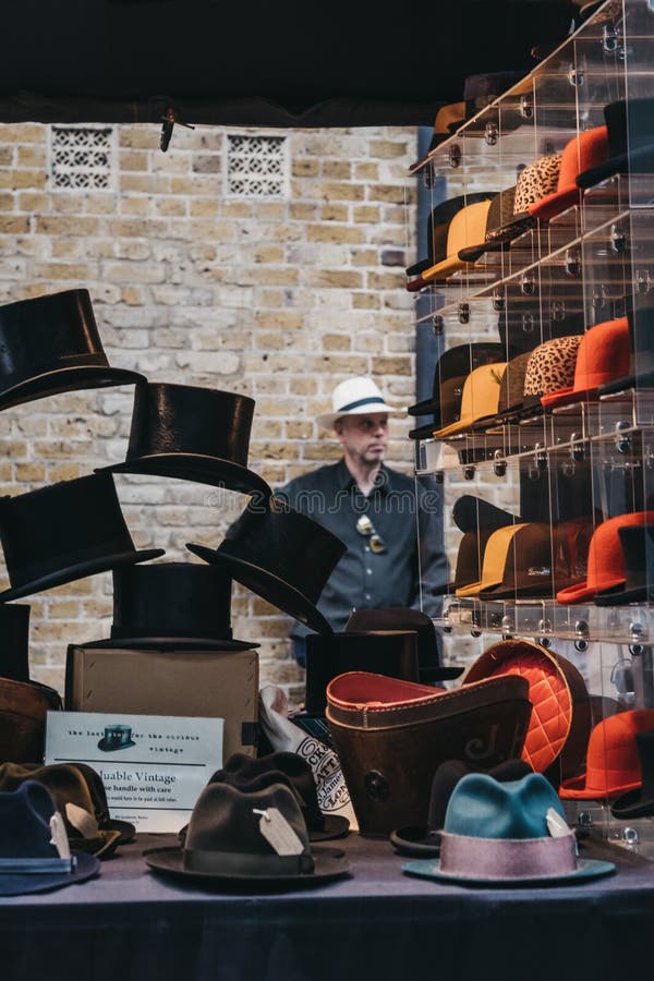 Άνδρας πίσω από καπέλα που πωλείται σε στάση στο Spitalfields Market,  Λονδίνο, ΗΒ Εκδοτική Στοκ Εικόνες - εικόνα από lifestyle: 151723698